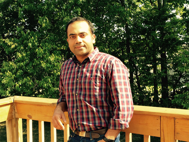Vamsi Patlolla stands in front of a wooden deck next to a forested area in the background.