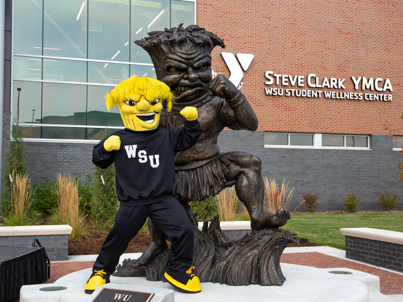 WuShock poses with his sculpture in front of the Steve Clark YMCA on Wichita State's campus