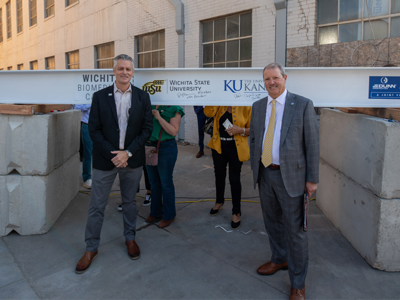 President Rick Muma and Doug Girod, chancellor of the University of Kansas pose in front of their signatures on the final beam for the Wichita Biomedical Campus construction