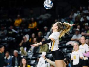A volleyball player prepares to spike a ball at a game in Charles Koch Arena in front of a crowd of people