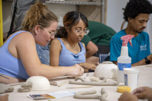 Three young people create ceramic bowls at a table.