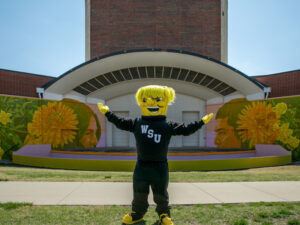 WuShock poses in front of the Adelante Juntos mural at the Duerksen Fine Arts Center Amphitheater