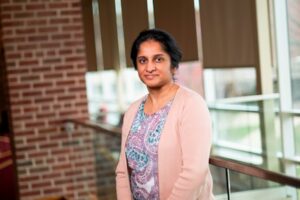 Photograph of Dr. Anuradha Ghosh leaning against a railing. She is looking at the camera with a subtle smile.