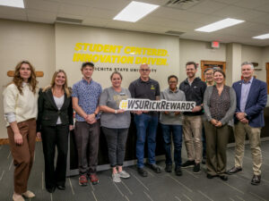 President Rick Muma poses with the Faculty Senate Executive Committee holding a sign that says Rick Rewards. The wall behind them says Student Centered, Innovation Driven.