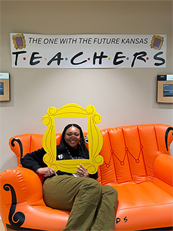 Trajata Colbert sitting underneath a banner which reads; the one with the future Kansas teachers.