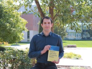 Dr. Tamás Molnár holding his book, "Dynamics and Control of Connected Vehicles"