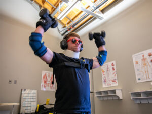 A physical therapy student at Wichita State University tests a homemade geriatric-simulation suit with wrist weights, dumbbells, elbow braces, sunglasses, earmuffs and a neck brace