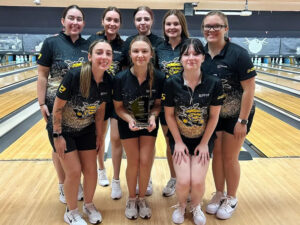 The Shocker women's bowling team pose in front of bowling lanes with its runner-up trophy