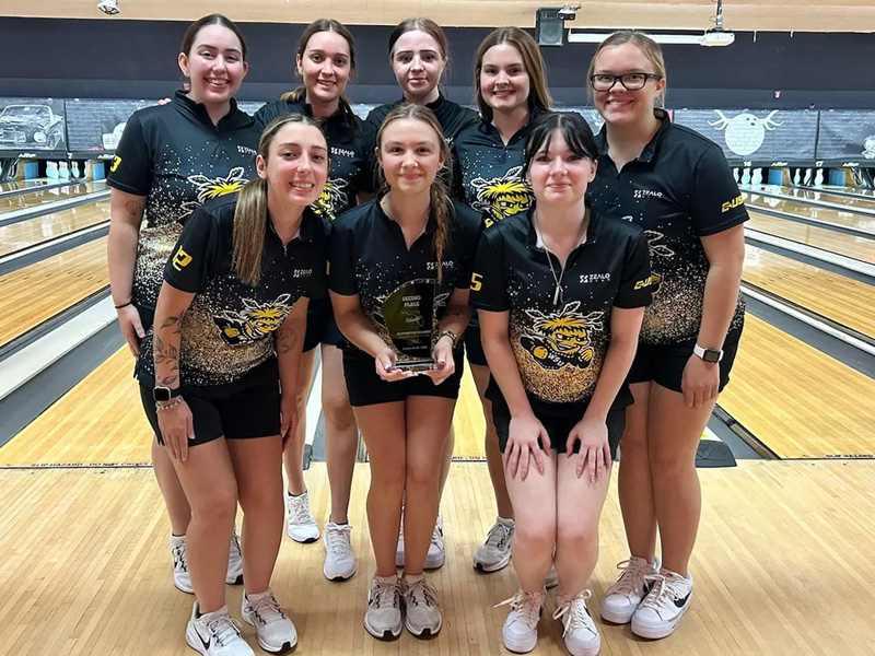 The Shocker women's bowling team pose in front of bowling lanes with its runner-up trophy