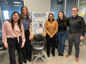 Five students pose with smiles in front of their open house poster and prototype, an ergonomic dental stool to reduce back pain for dental hygienists.