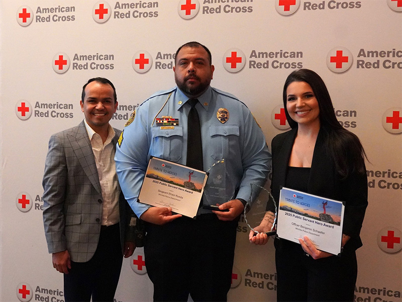 Efrain Rueda holds up his award in front of an American Red Cross backdrop and representatives from the American Red Cross
