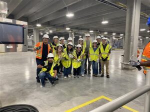 A group of students wearing hard hats and safety vests pose in a water treatment plant with pipes and machinery.