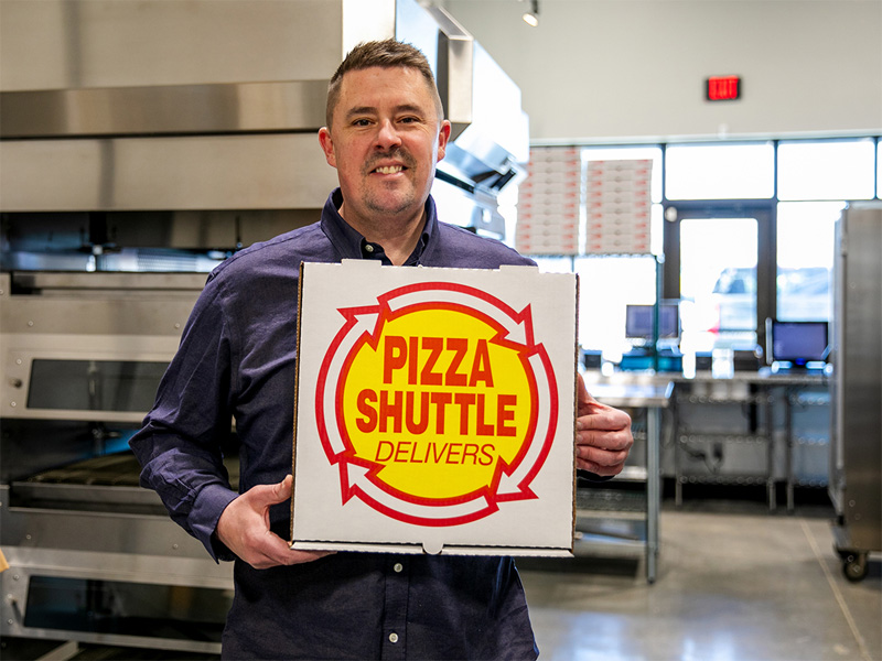 Justin Neal holds up a Pizza Shuttle pizza box