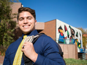A student in a blue button up shirt and a WSU tie poses in front of the Ulrich Museum of Art