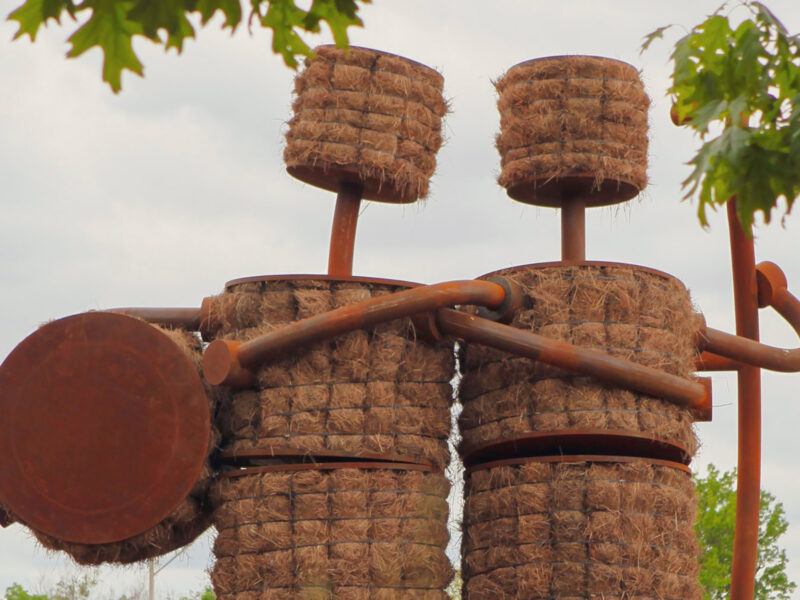 The sculpture, Shockers by Tom Otterness, is a Corten steel frame filled with hay that forms the figures of two friends.