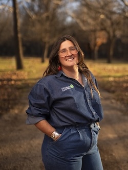 Photograph of Zoë Colatarci. She is smiling at the camera with her hands in her pockets.