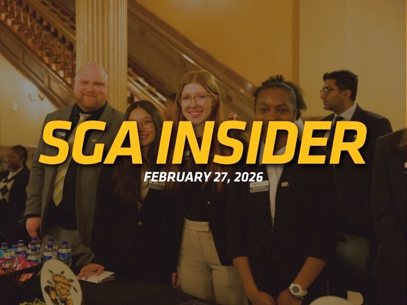 Four students in professional attire stand behind a table at a campus event, smiling toward the camera in a formal indoor setting with a staircase and columns in the background. Large yellow text across the image reads “SGA Insider,” with smaller white text below reading “February 27, 2026.”