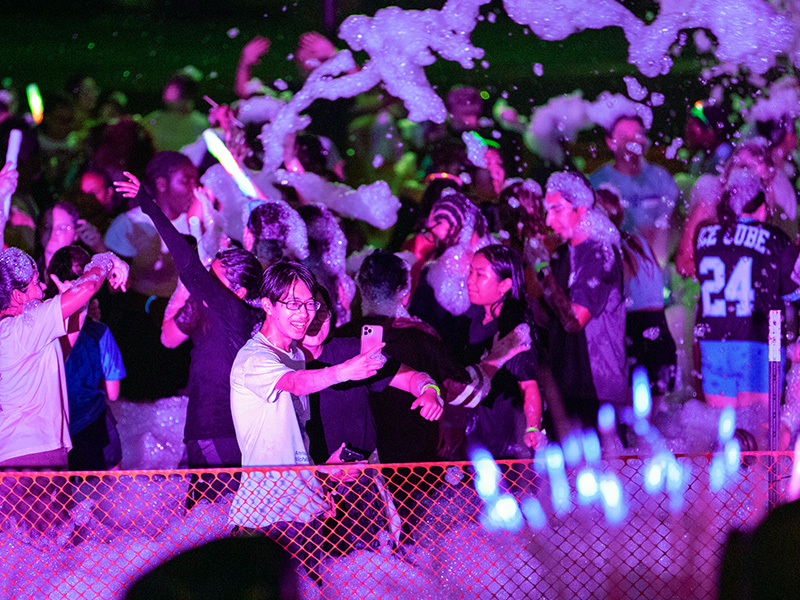 Students take part in the foam party at night with a purple light shining across them