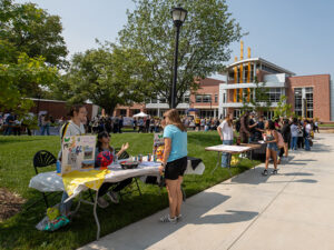 A student visits a women's soccer table in front of the Rhatigan Student Center with many students in the background visiting other student organization tables