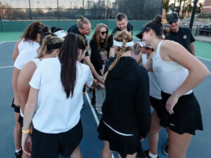 The women's tennis gather together in a circle to celebrate a win