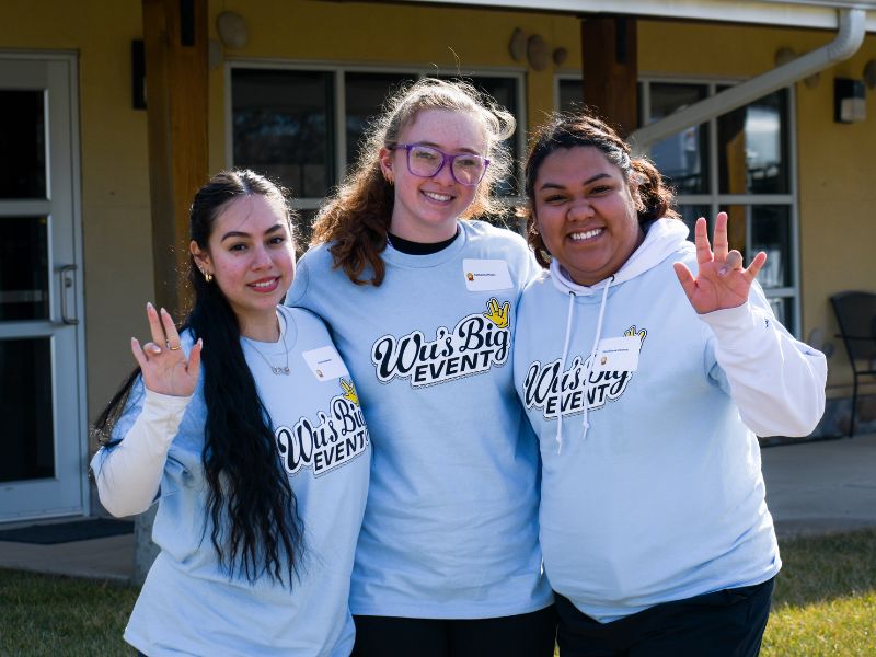 Three student volunteers standing and posing arm in arm.