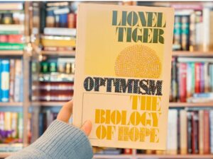 Image of a hand holding a bedazzled book titled "Optimism: The Biology of Hope" by Lionel Tiger.
