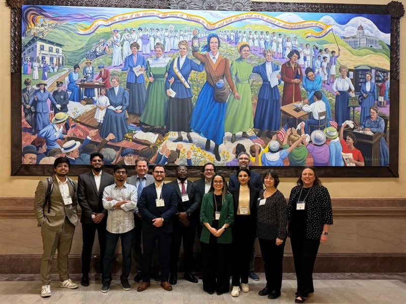 Group picture of WSU students who presented their research in Topeka. they are posing in front of a huge painting at the Kansas Capitol.