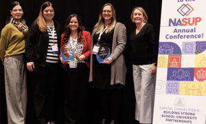 Representatives from Wichita State University and Wichita Public Schools hold up awards next to a sign for the NASUP annual conference and the 2026 Exemplary School-University Partnership Award from the National Association for School-University Partnerships (NASUP)