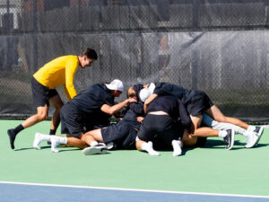 The men's tennis team huddles together in celebration after the upset win against Oklahoma State