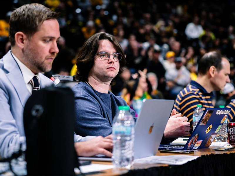 Owen Prothro sits at the press table in Charles Koch Arena during a men's basketball game