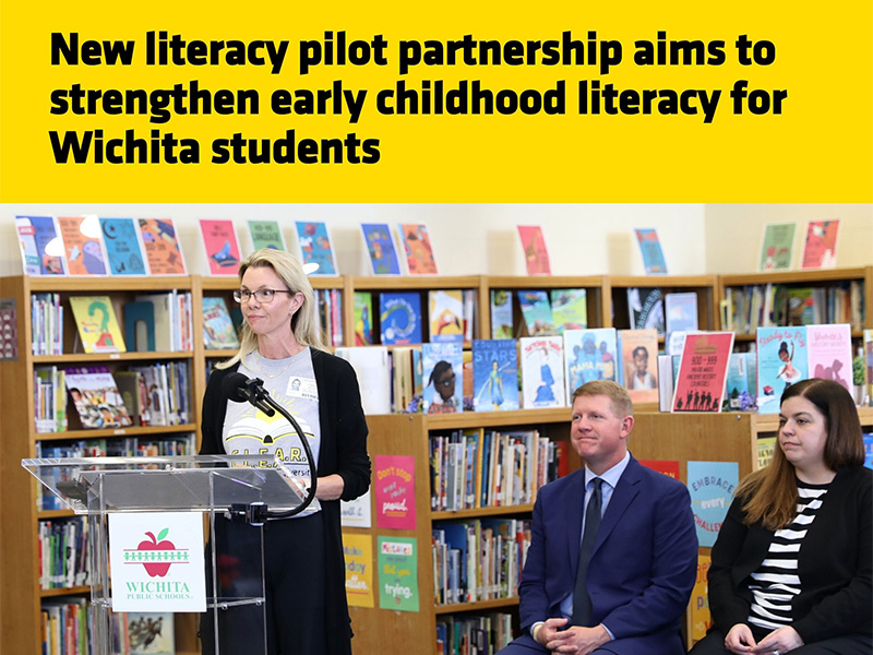 Dr. Kim Moody speaks at a podium with a Wichita Public Schools logo during a press conference in an elementary school library. The event announced a new literacy pilot partnership focused on strengthening early childhood literacy for Wichita students.