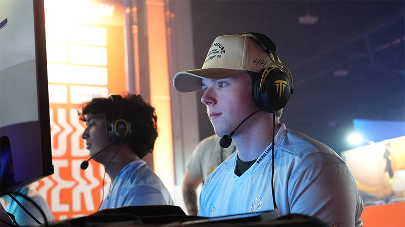 Two Wichita State esports players compete at gaming stations, wearing headsets and team jerseys while focused on their screens during a Rocket League match.