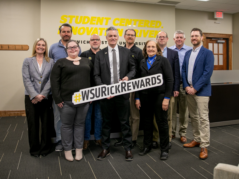 President Rick Muma poses with a sign that says WSU Rick Rewards and members of the interdisciplinary group that were awarded this month