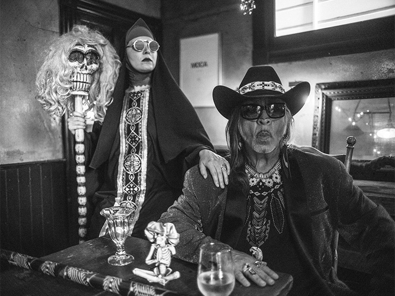 A women in a long dress and a serious looking man pose in a bleak room.