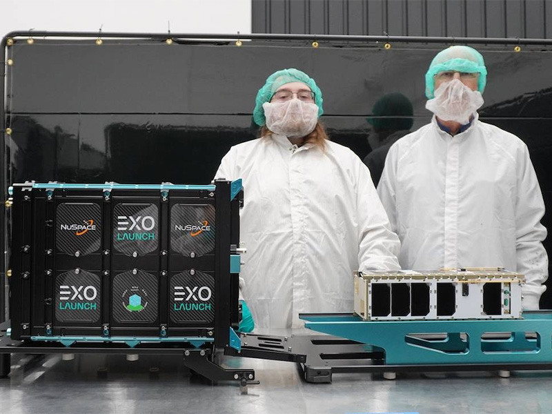 A student and a scientist in full clean garb stand next to the WSU CubeSat
