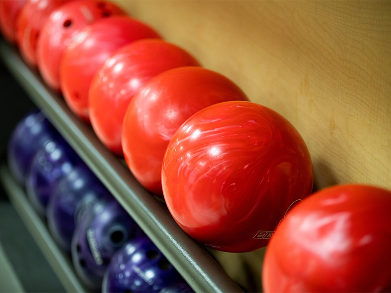 Red bowling balls on a top rack with blue bowling balls on the lower rack