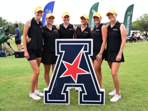 Members of the Shocker women's golf team pose behind the American Conference logo in a grassy field