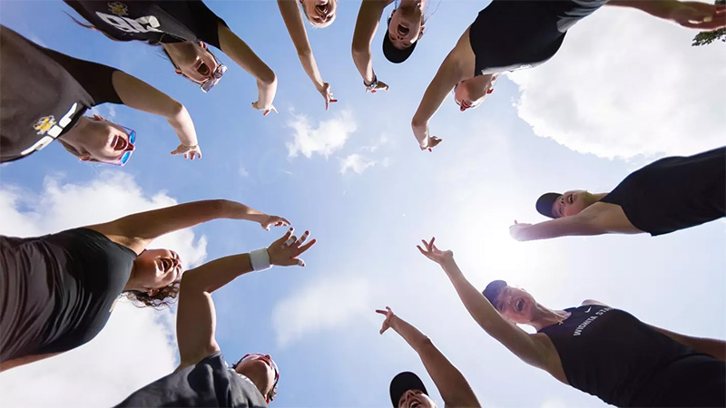 The women's tennis team huddles in a circle and gives the Shocker hand sign.