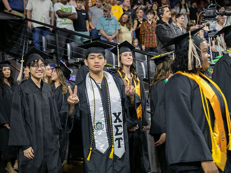 A student gives the peace sign with his hands at a commencement ceremony at Wichita State