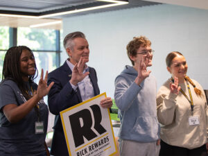 President Rick Muma poses with students while holding a Rick Rewards sign as they all hold up the Shockers hand sign
