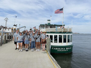 The group of students who went on the trip pose in front of a boat on the coast of Charleston, South Carolina