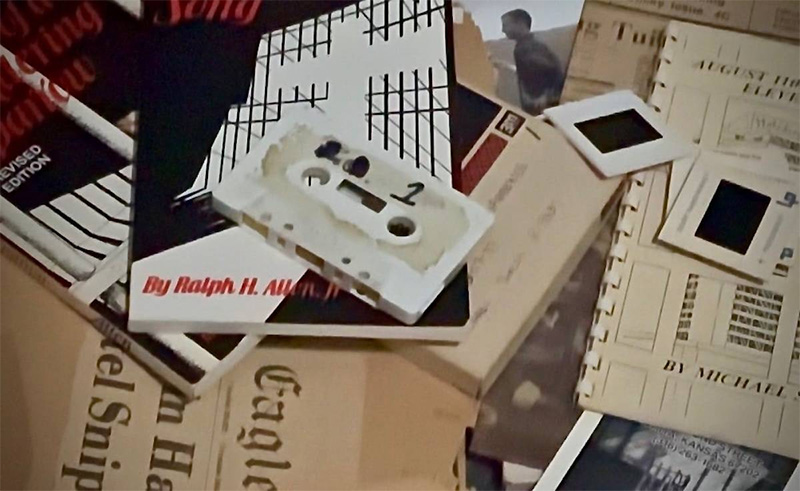 A still from the documentary showing various documents, books tapes and photos.