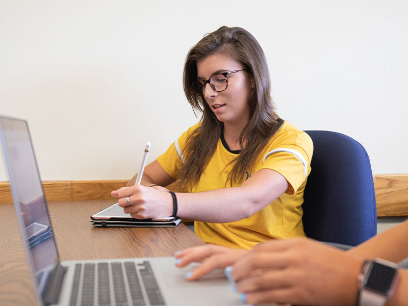 A student takes a proctored exam at a desk