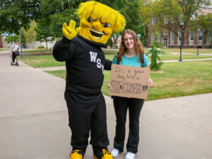WuShock poses with a student holding up a cardboard sign that reads "It's a great day to be a Shocker!"